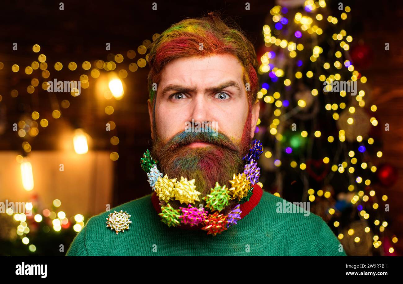 Christmas beard decorations. Surprised man with decorated beard for New year or Christmas party. Closeup portrait of bearded man with dyed hair and Stock Photo