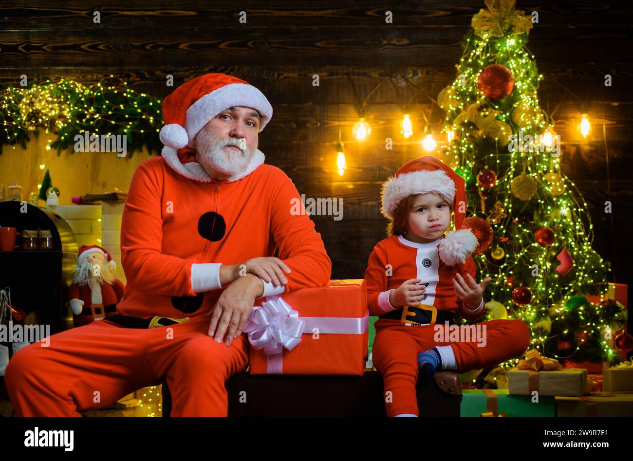 Winter holiday. Christmas decoration. Santa Claus with little helper near Christmas tree. Santa man and funny child boy with Christmas gift. New Year Stock Photo