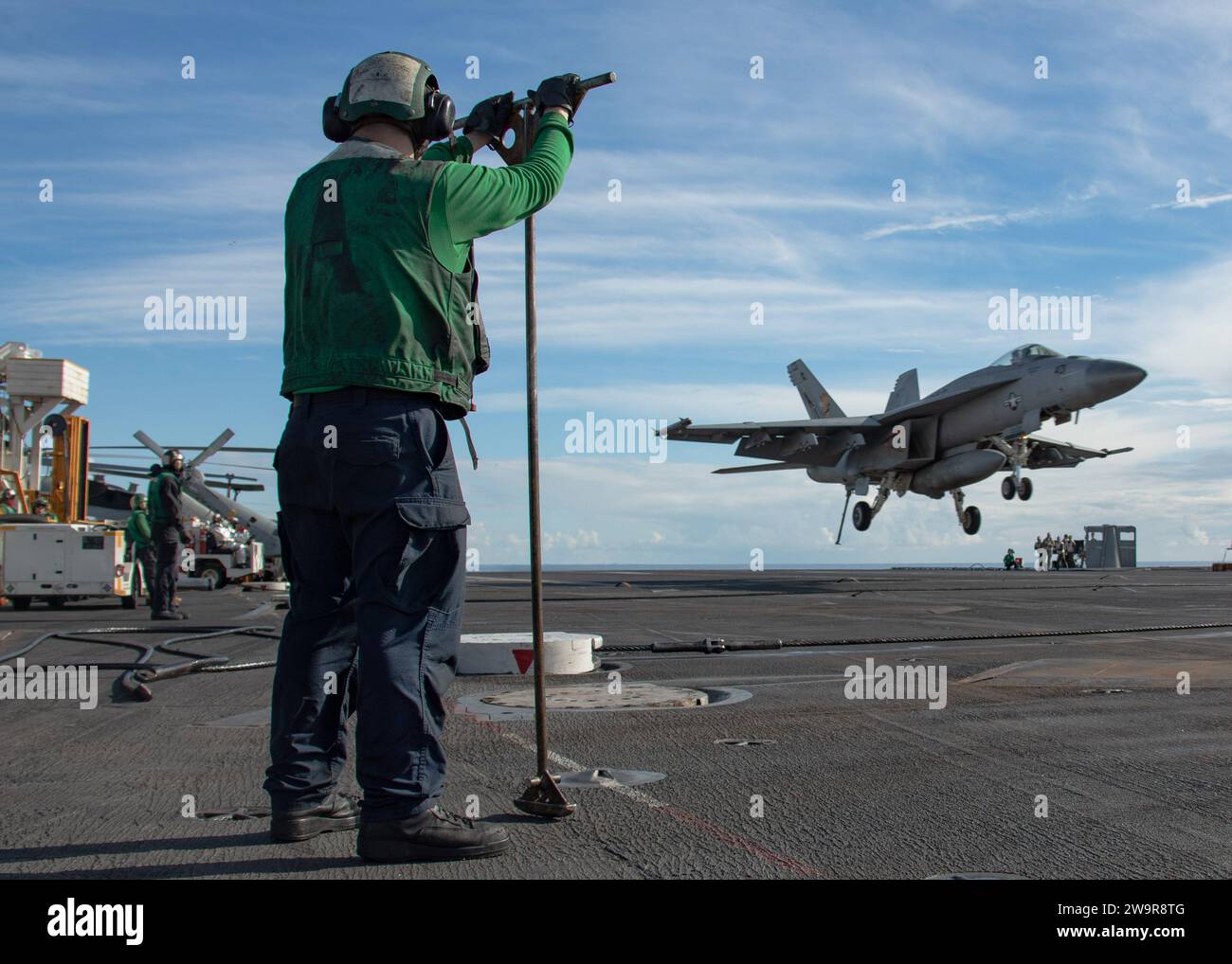 Aviation Boatswain's Mate (Equipment) 3rd Class Domnic Tse, assigned to the air department of the worldÕs largest aircraft carrier USS Gerald R. Ford (CVN 78), prepares for an F/A-18E Super Hornet, attached to the 'Golden Warriors' of Strike Fighter Squadron (VFA) 87, to land on the flight deck during routine operations, Dec. 11, 2023. The Gerald R. Ford Carrier Strike Group is currently operating in the Mediterranean Sea. The U.S. maintains forward deployed, ready, and postured forces to deter aggression and support security and stability around the world. (U.S. Navy photo by Mass Communicati Stock Photo