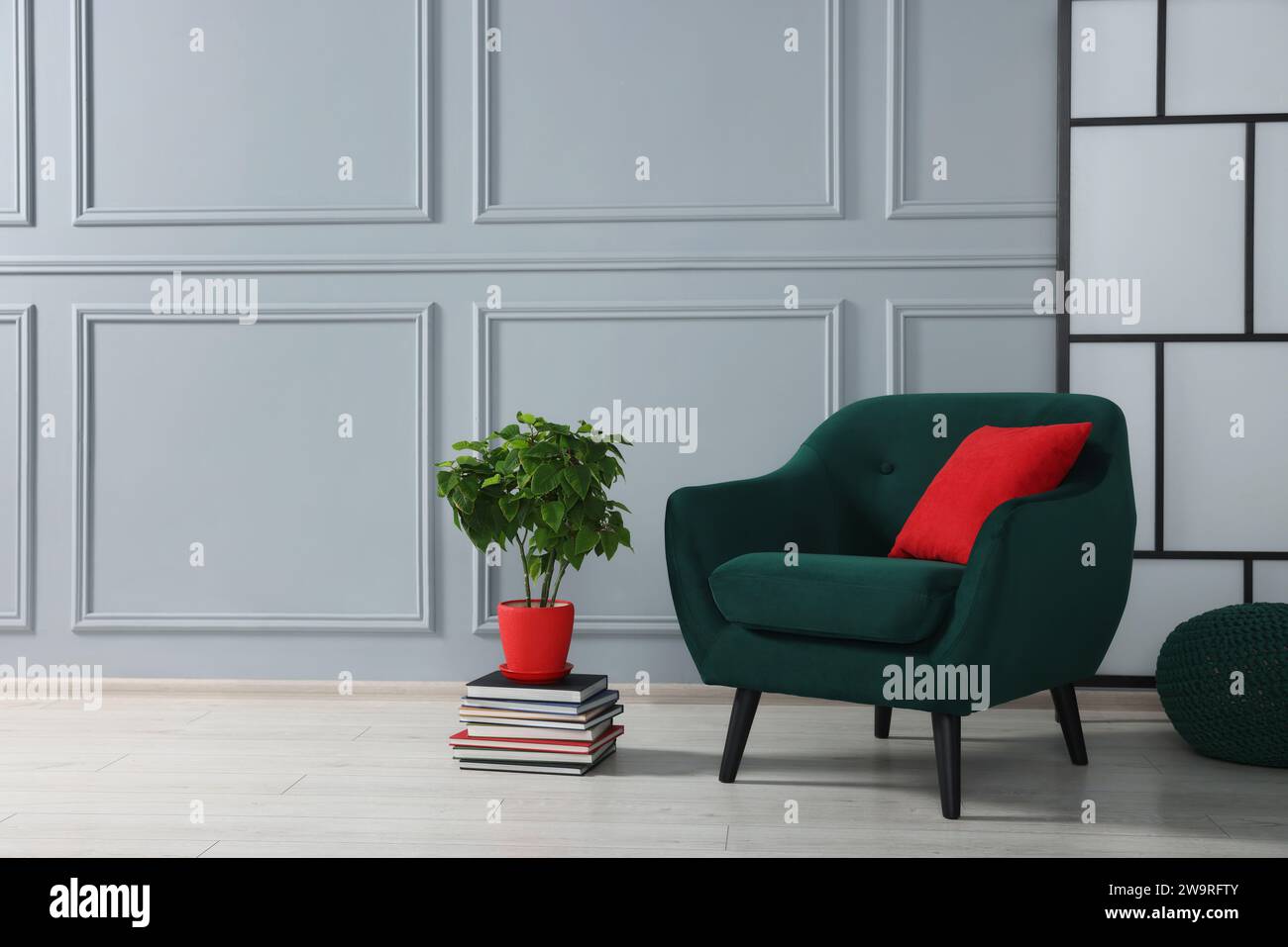Stylish armchair with pillow and houseplant on floor near light grey ...