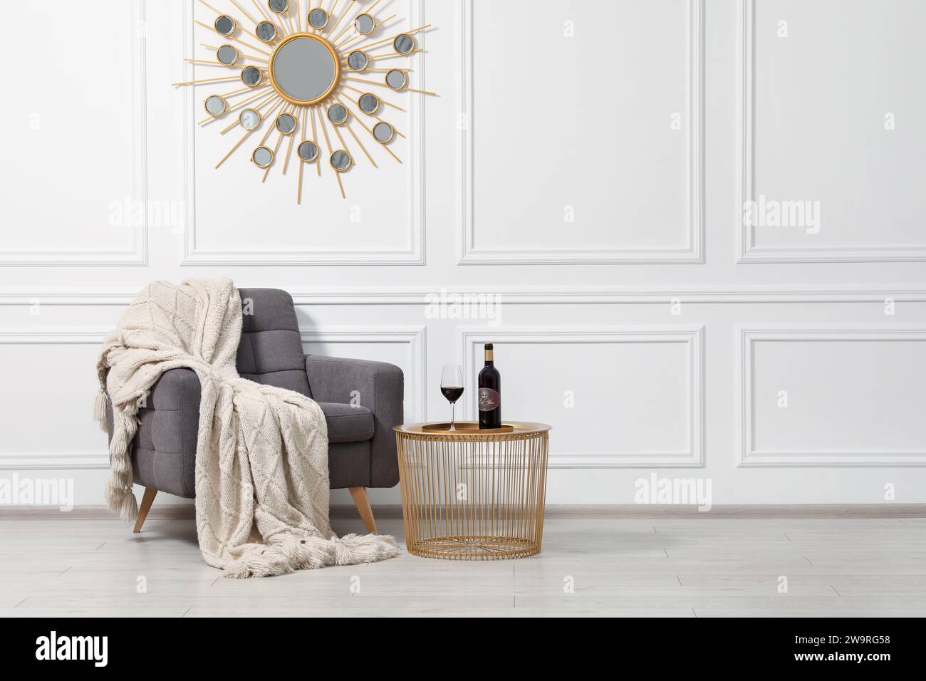 Comfortable armchair, blanket and wine on side table near white wall ...