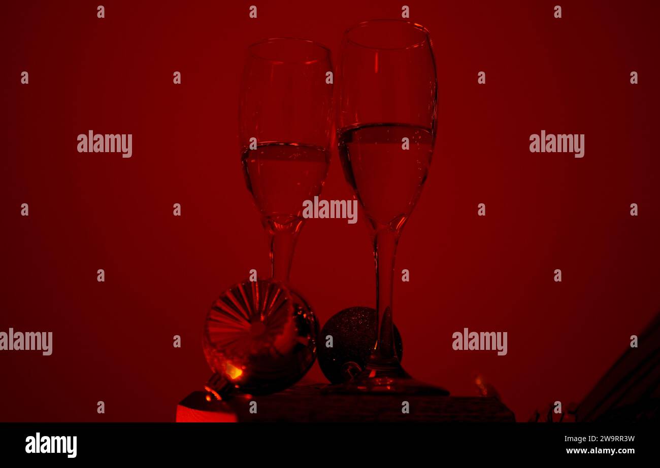 Red background, two stemmed glasses of champagne, Christmas ornaments Stock Photo