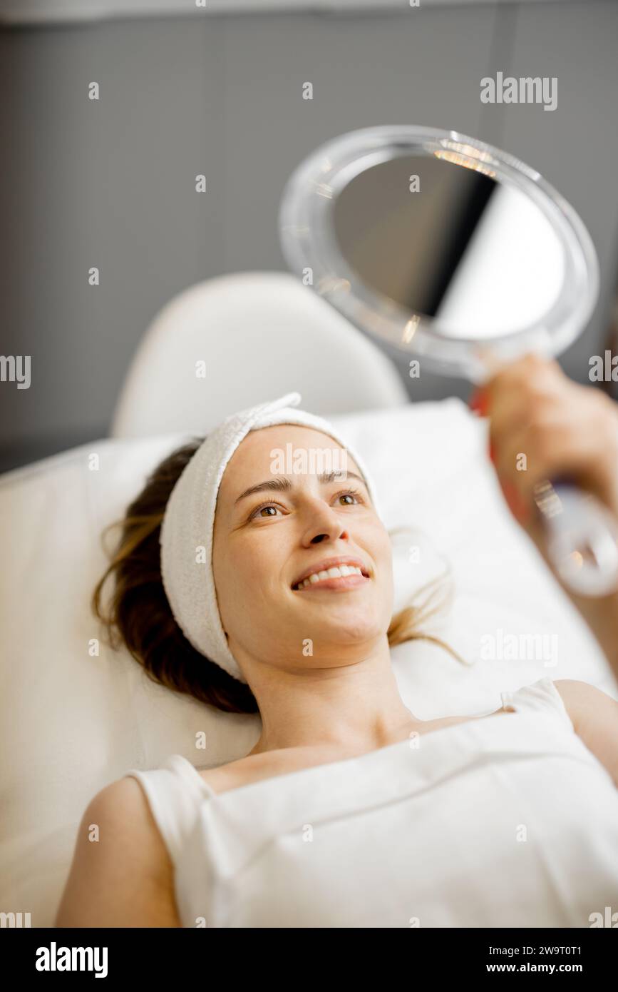 Happy woman looks on her face at beauty salon Stock Photo