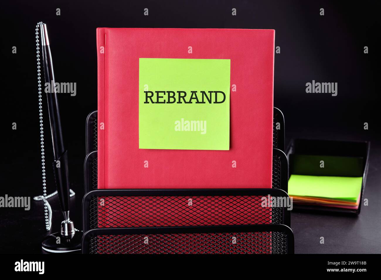 REBRAND Text on a yellow sticker on a red vertical notepad on a black background next to a pen and money Stock Photo