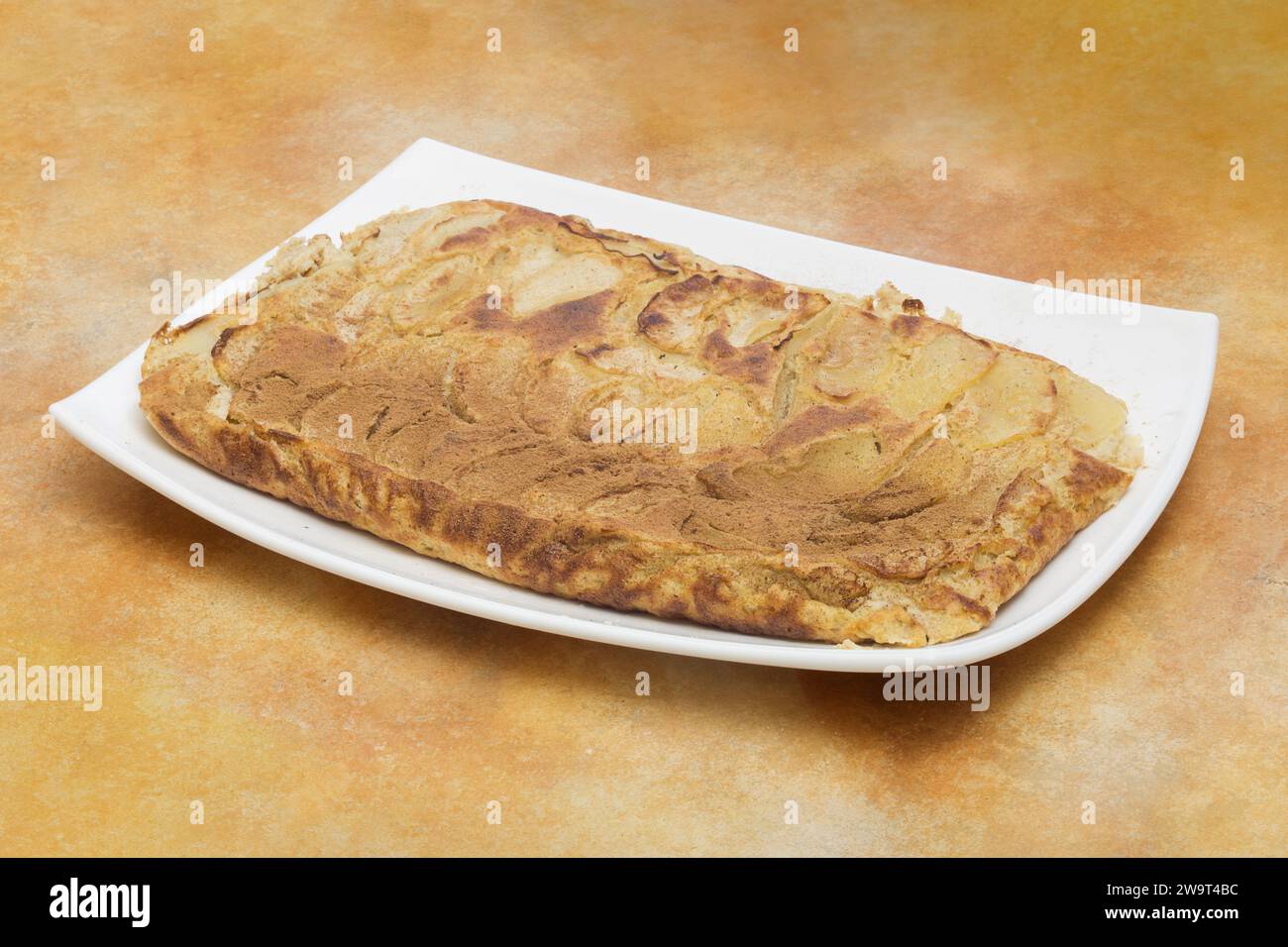 A beautifully baked apple pie with cinnamon on it, presented on a white, rectangular plate with a golden brown crust and tantalizing glimpses of the a Stock Photo