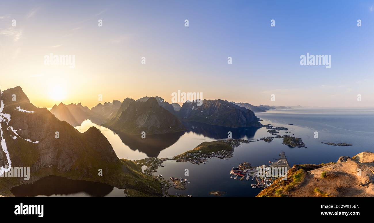 The midnight sun casts its ethereal glow over a super panorama seen from Reinebringen; a wide-angle perspective shows the dramatic Lofoten peaks surro Stock Photo