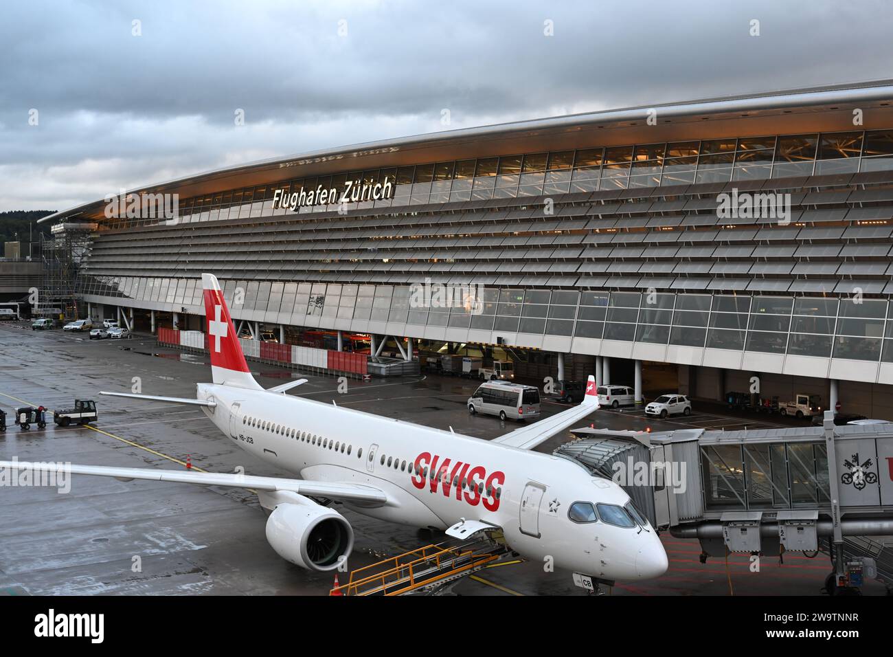Plane from Swiss company is parked in Zurich airport. Airplane is connected to pull out arm or connector for embarking of passenger. Stock Photo