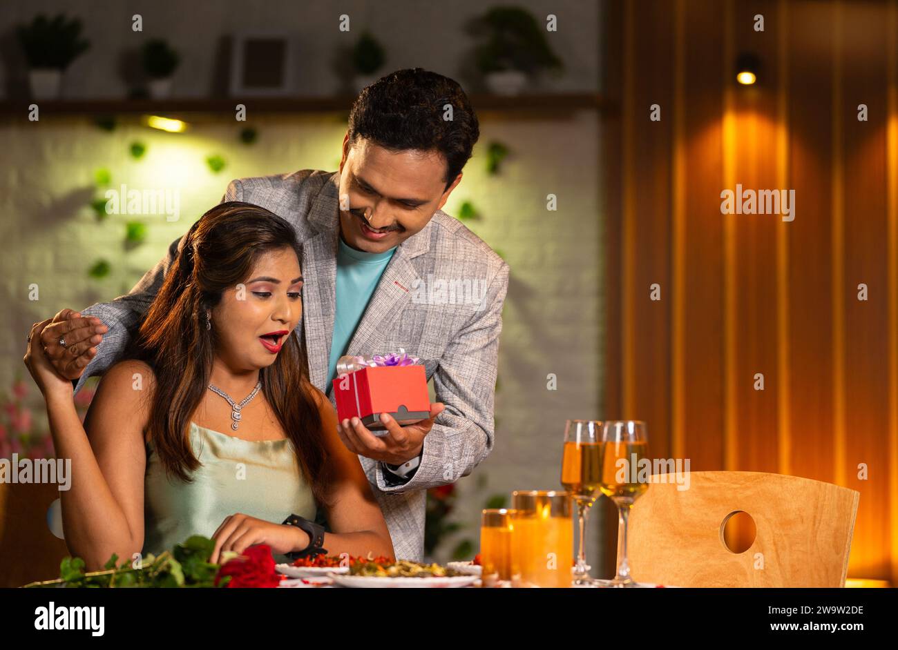 happy husband giving surprise gift to wife at candlelight dinner for anniversary or birthday
