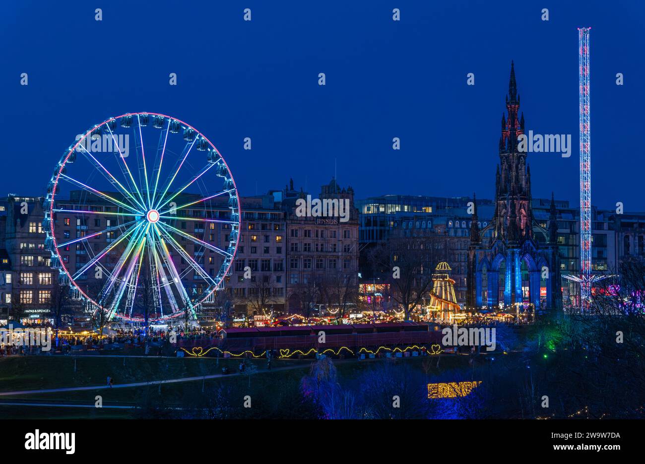 Big ferris wheel and star flyer fairground rides lit up at night at