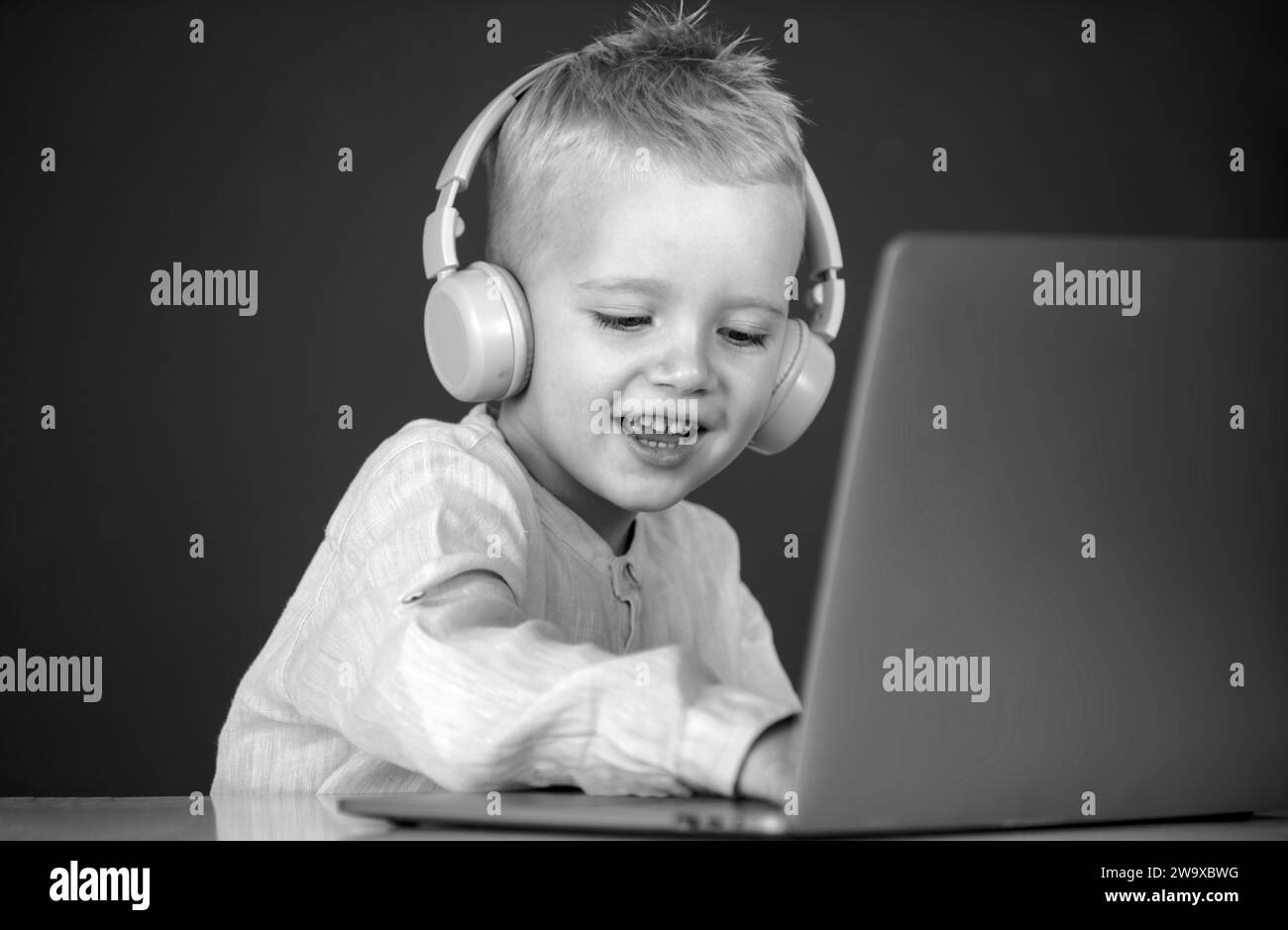 Clever school boy, cute pupil wears headphones writing on laptop ...