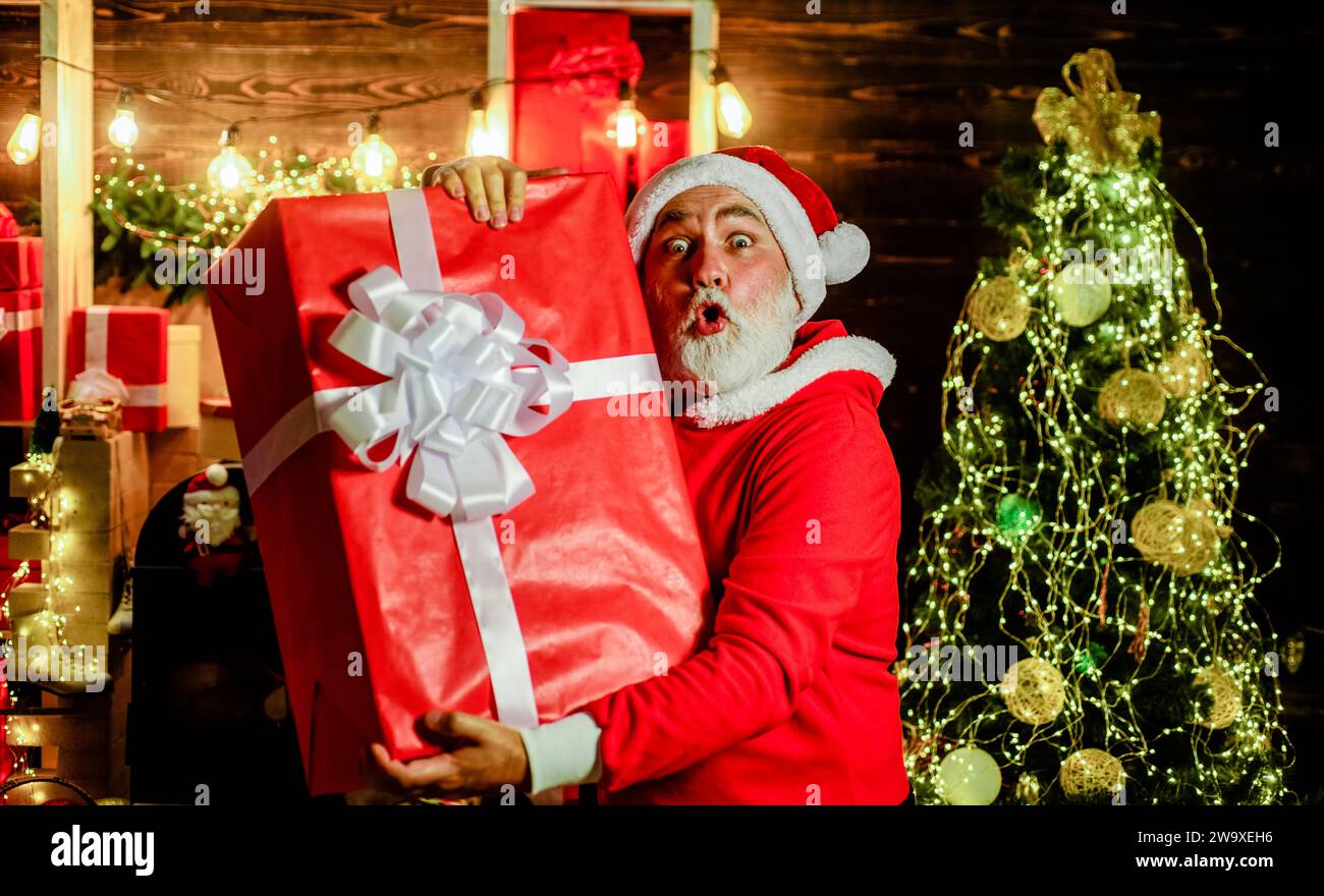Surprised Santa Claus with Christmas gift box in room decorated for Christmas. Winter family holidays. Christmas and New Year celebration. Bearded man Stock Photo