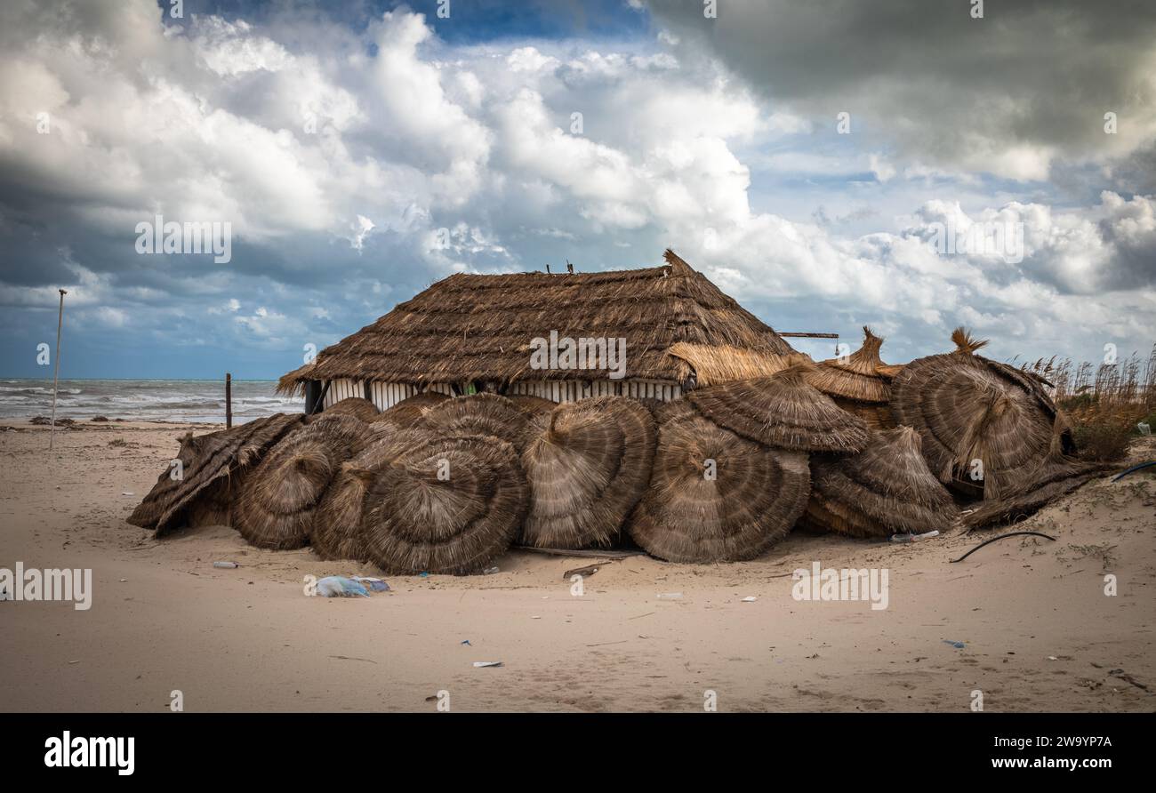 An abandoned store hut and piles of thatched parasols on the litter-strewn Samara Beach in Sousse, Tunisia Stock Photo
