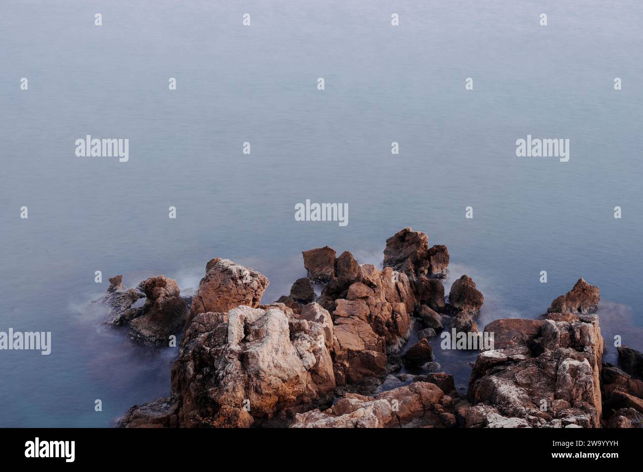 Antibes, France. December 30, 2023. Sea rocks photographed at sunset in front of the medieval walls of Antibes Stock Photo