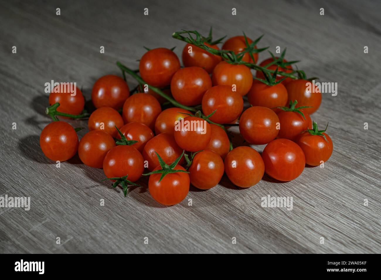 A group a bunch of loose and clustered whole raw cherry tomatoes on a wooden table Stock Photo