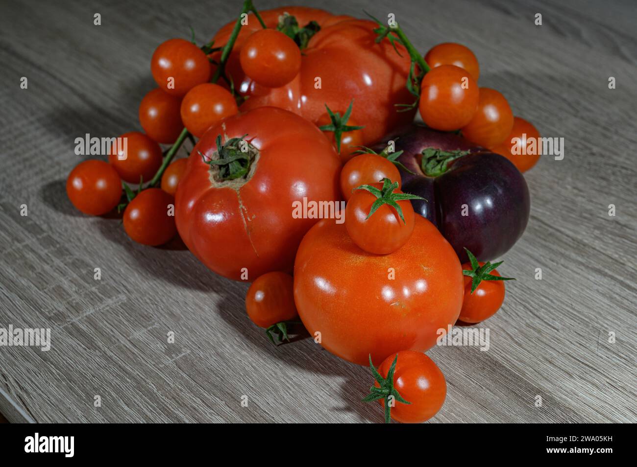 A group a bunch of whole raw tomatoes of several different types, blue, red, cherry tomatoes and a large pink tomato on a wooden table Stock Photo