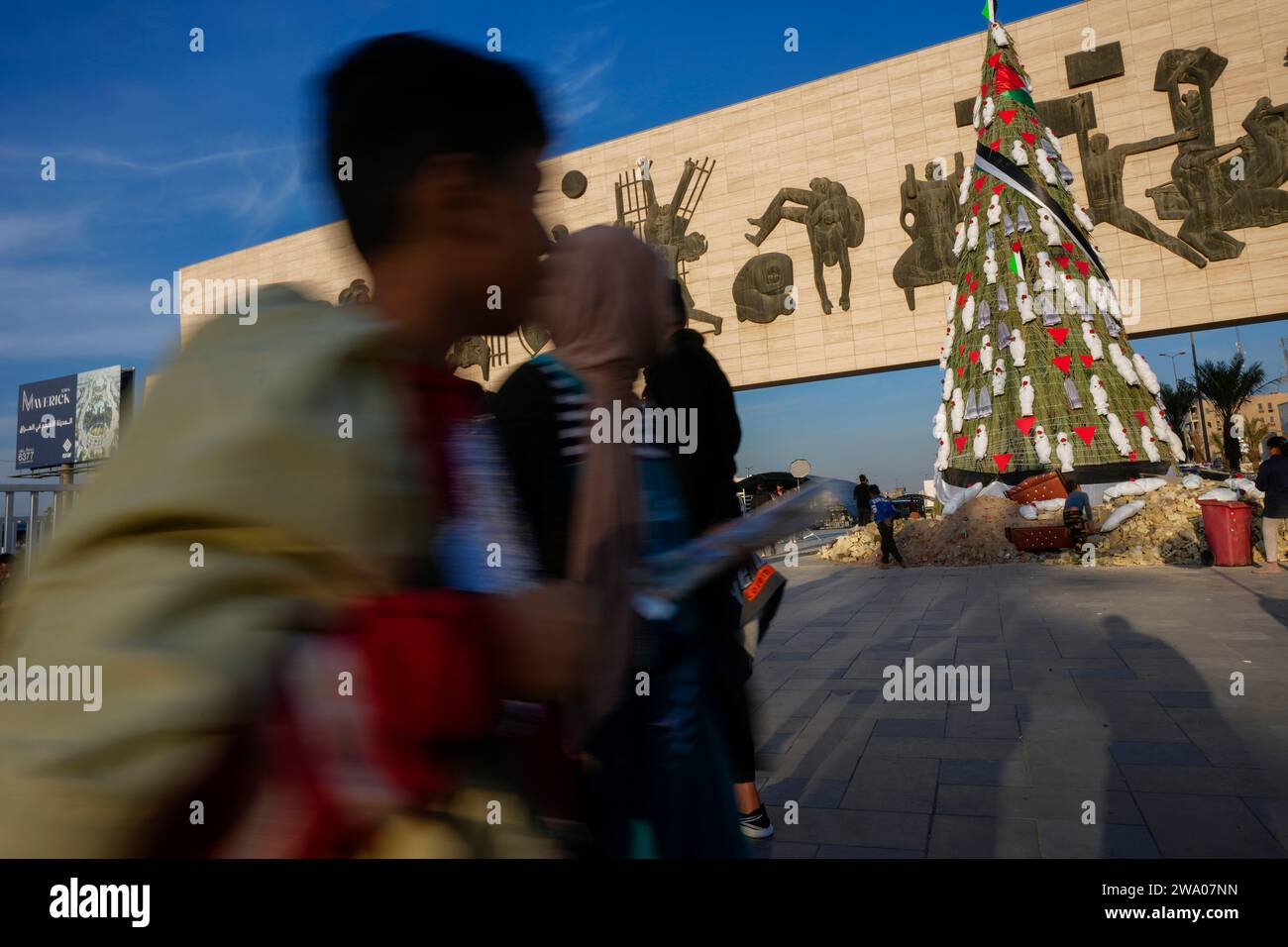 Iraqis stroll around a Christmas tree decorated with items resembling children wrapped in shrouds in a display of solidarity with Palestinians in Gaza, at Tahrir Square in Baghdad, Iraq, Sunday, Dec. 31, 2023. (AP Photo/Hadi Mizban) Stock Photo