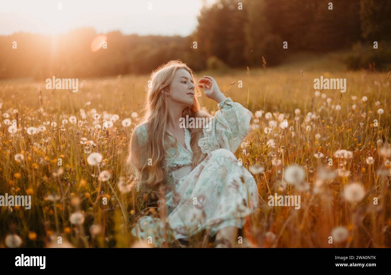 A beautiful young blonde woman with long hair in a white dress walks ...
