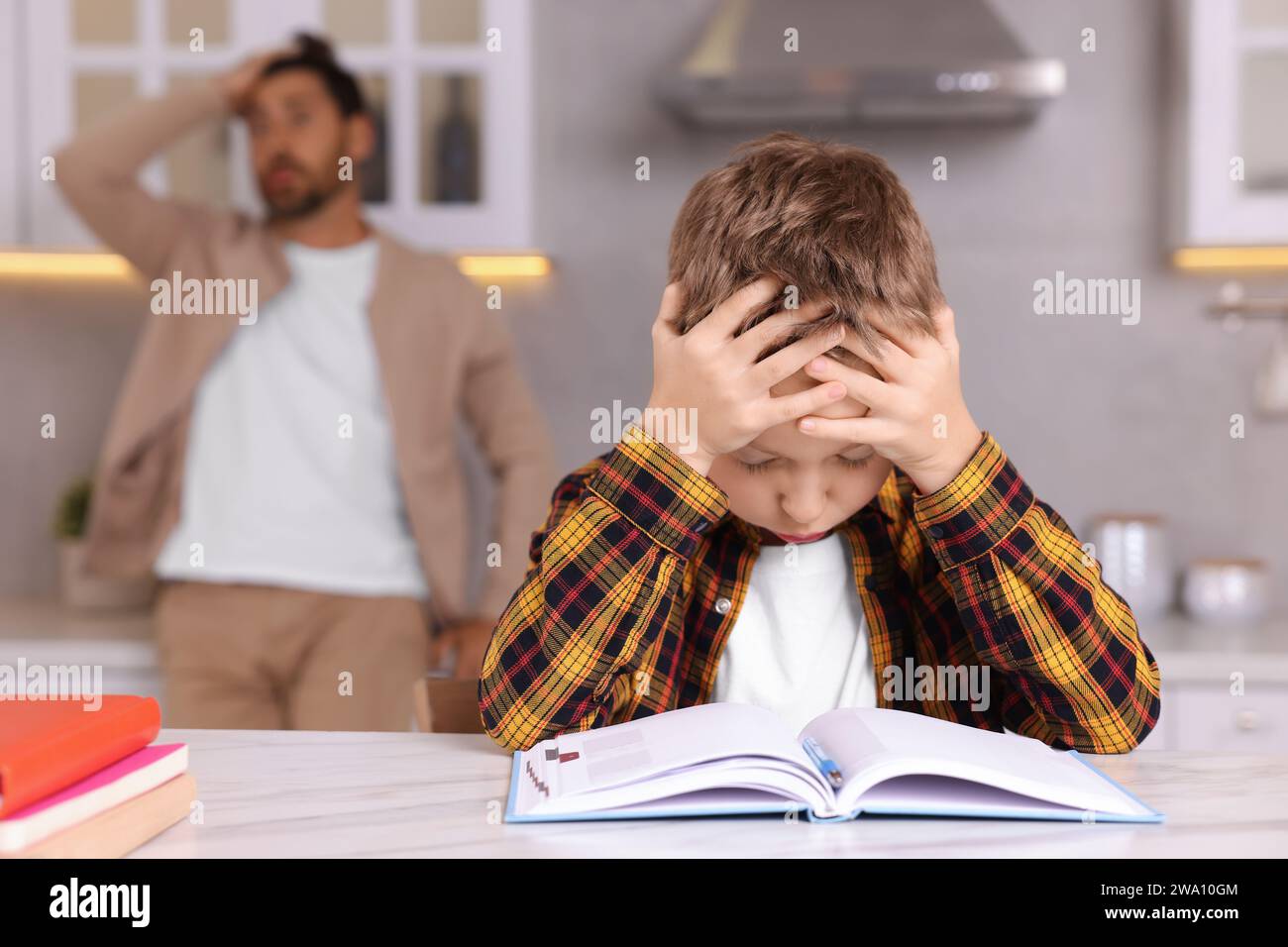 Father getting annoyed while son doing his homework in kitchen, selective focus. Dyslexia problem Stock Photo
