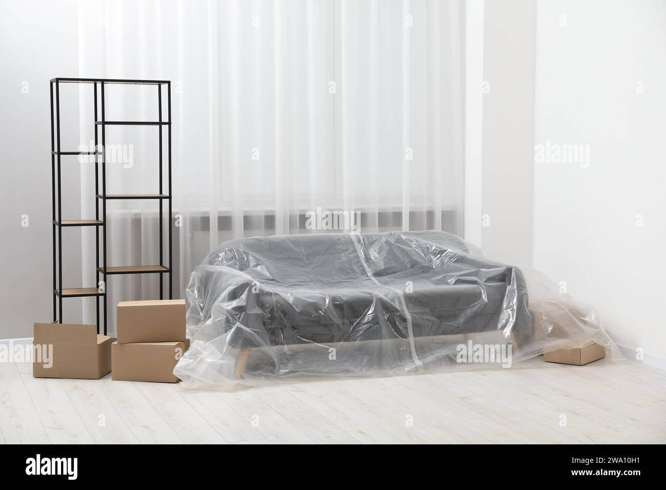 Stylish sofa covered with plastic film, shelving unit and boxes at home Stock Photo