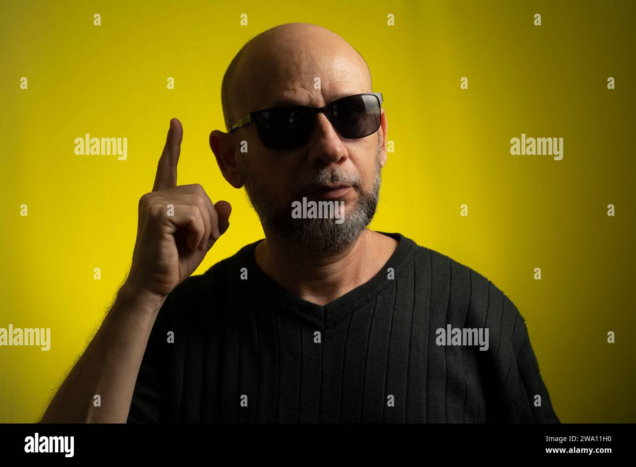 Portrait of bald, bearded mature man wearing sunglasses making sign with his hands. Isolated on yellow background. Stock Photo