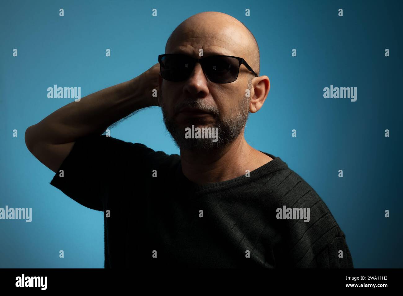 Portrait of bald and bearded mature man wearing sunglasses looking towards the camera. Isolated on blue background. Stock Photo