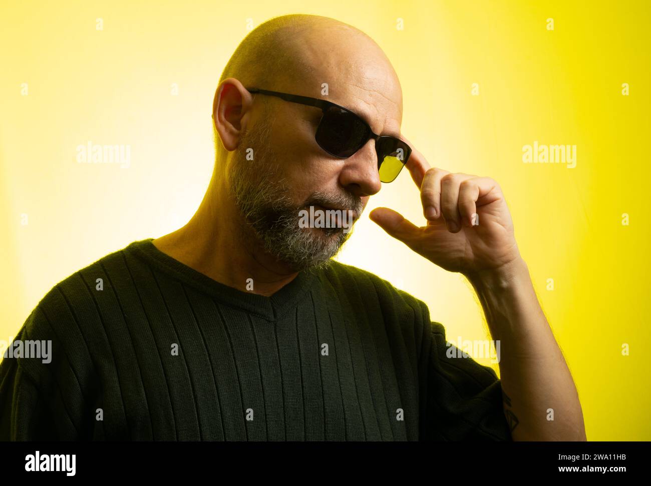 White man, bald, wearing sunglasses, serious and thoughtful. Isolated on yellow background. Stock Photo