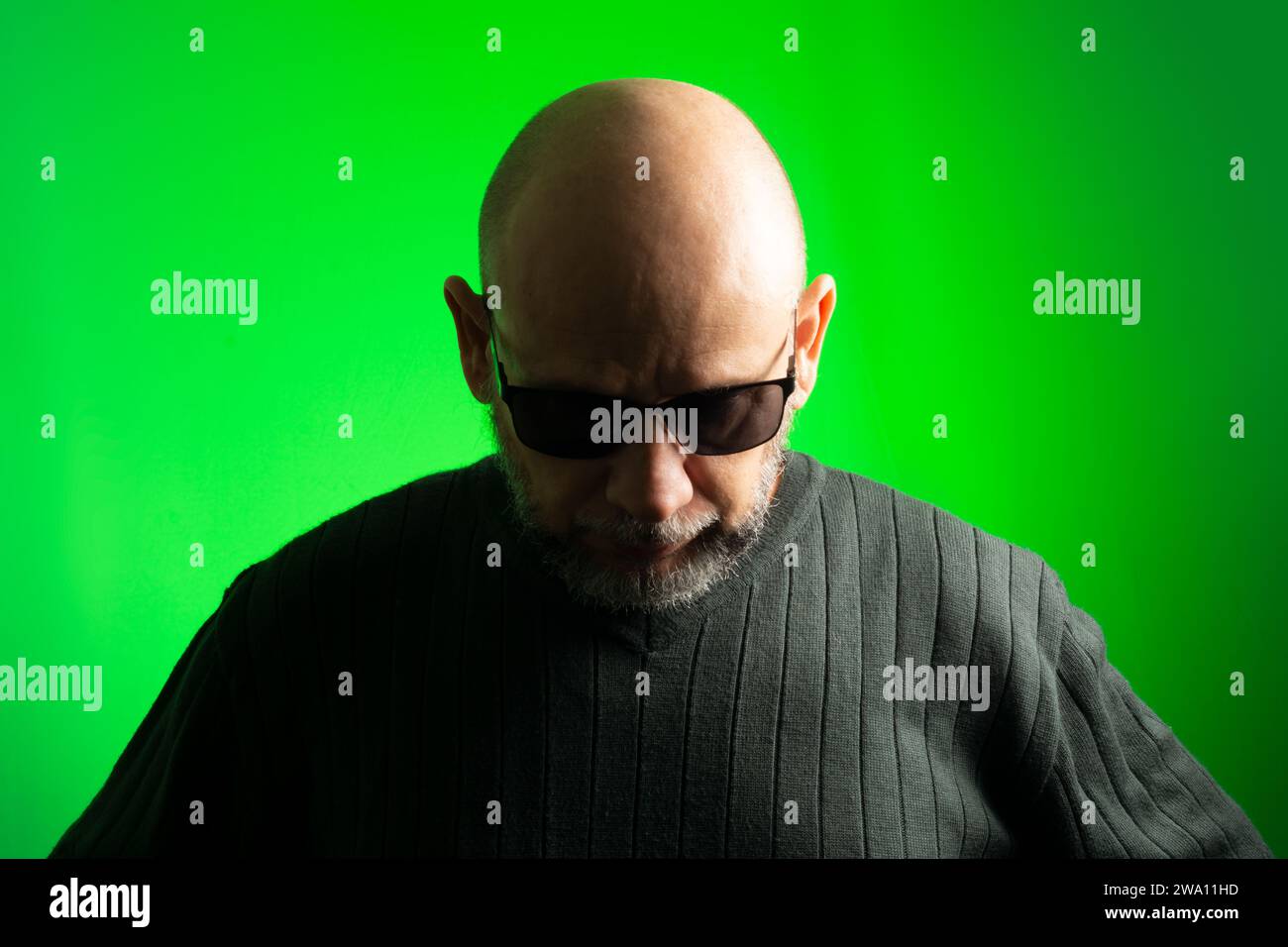 White man, bald, wearing sunglasses, serious and thoughtful looking down. Isolated on green background. Stock Photo