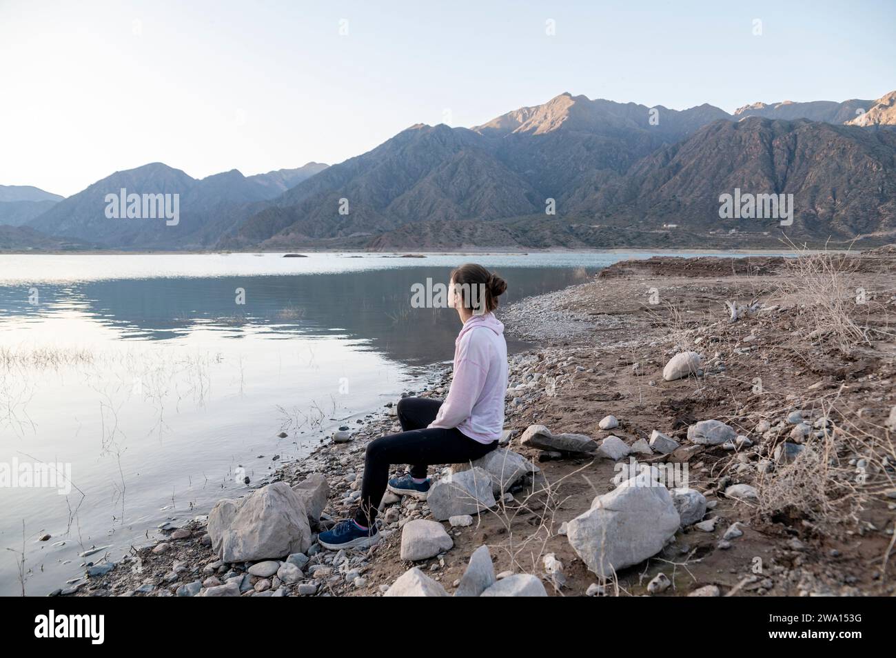 Woman meditating on the shore of a lake while enjoying the nature landscape. Stock Photo