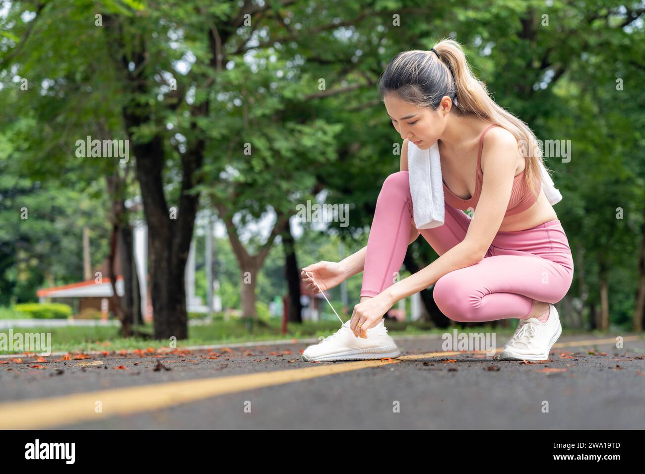 Young attractive Asian woman tying her shoelace before her morning exercise run at a running track of a local park Stock Photo