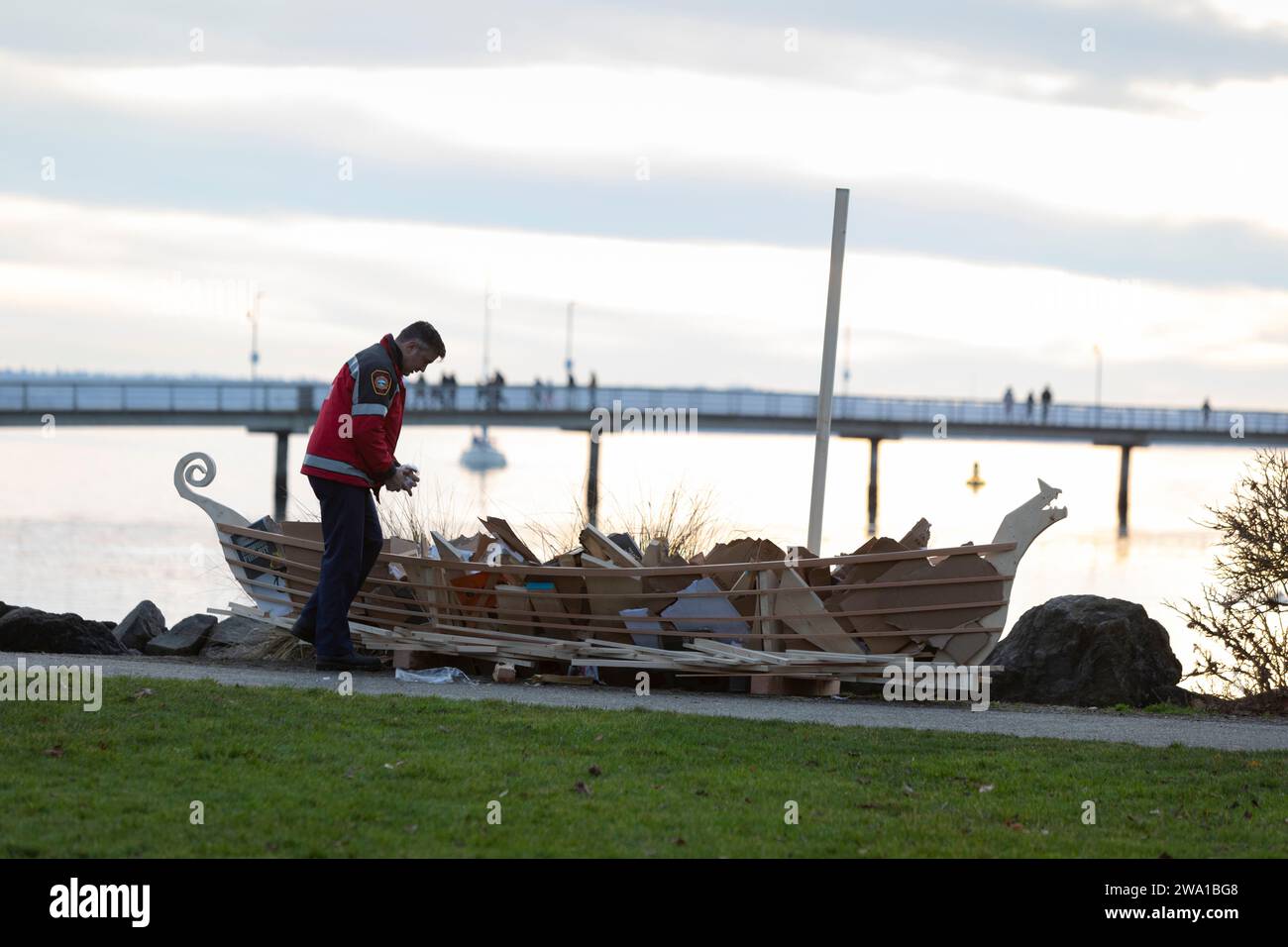 Des Moines, Washington, USA. 31 December, 2023. An officer with the South King Fire and Rescue prepares ceremonial boat at the Burning Boat Festival at Des Moines Beach Park. People were invited to write notes of personal goals for the new year or sorrows that need purging from the universe that will be placed in the boat. Credit: Paul Christian Gordon/Alamy Live News Stock Photo