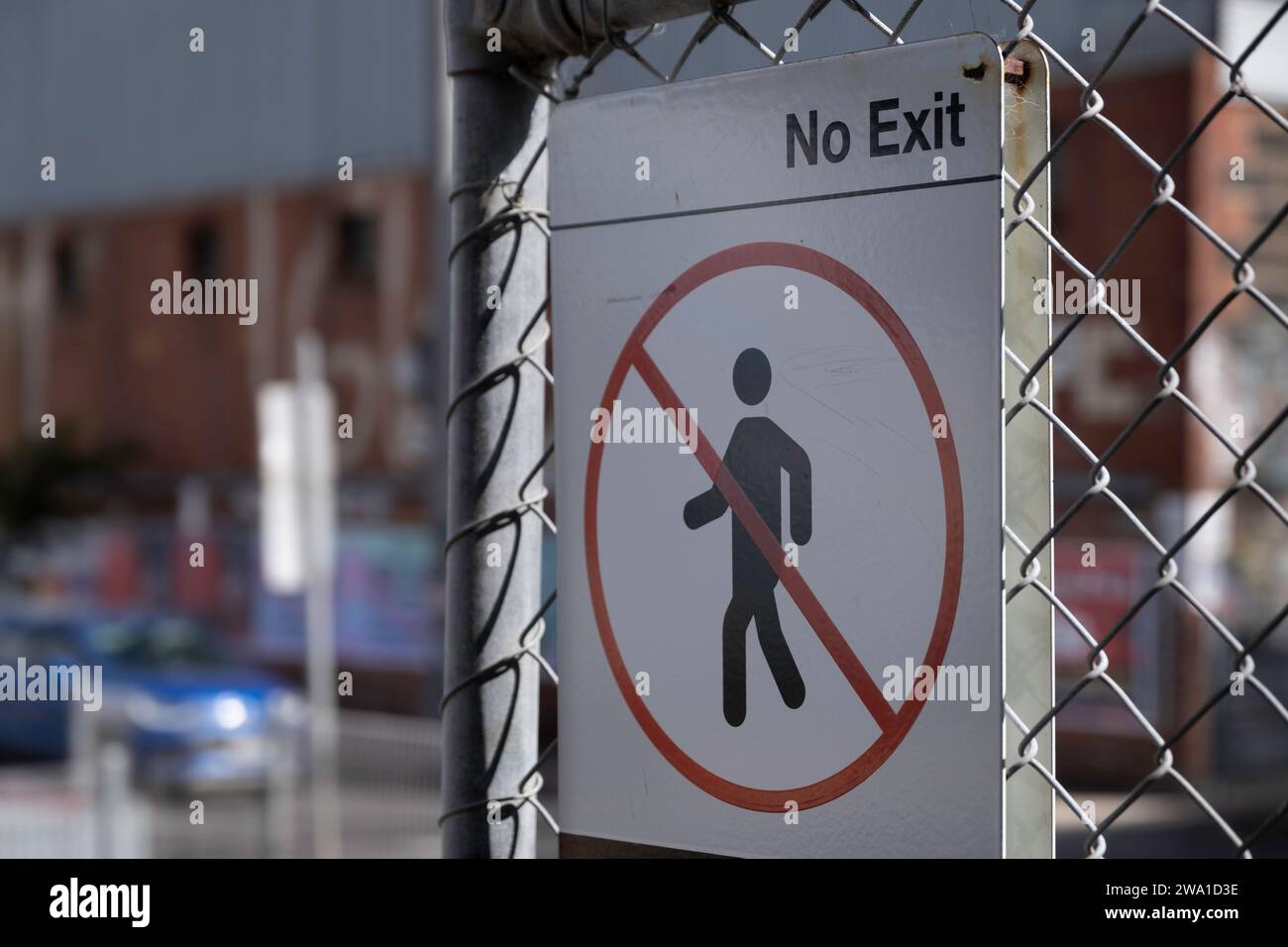 No exit sign mounted on a chain-link fence. Exit area prohibited sign. Blurred background of a road, car and building Stock Photo