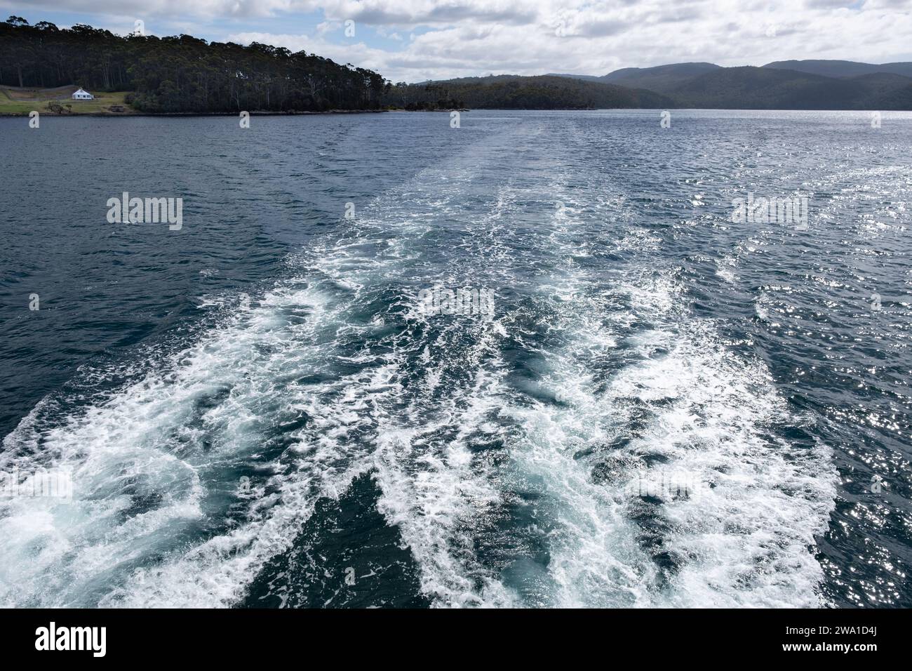 Stern waves from a boat sailing across Carnavon Bay with the Master Shipwright's House in the Port Arthur Penal Colony in Tasmania, Australia Stock Photo