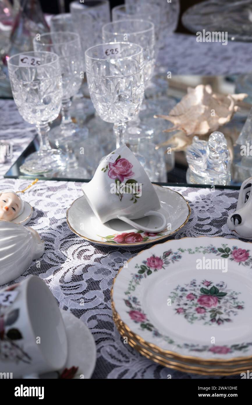Antique crockery with floral pattern and glassware displayed on a decorated tablecloth at an antique market Stock Photo