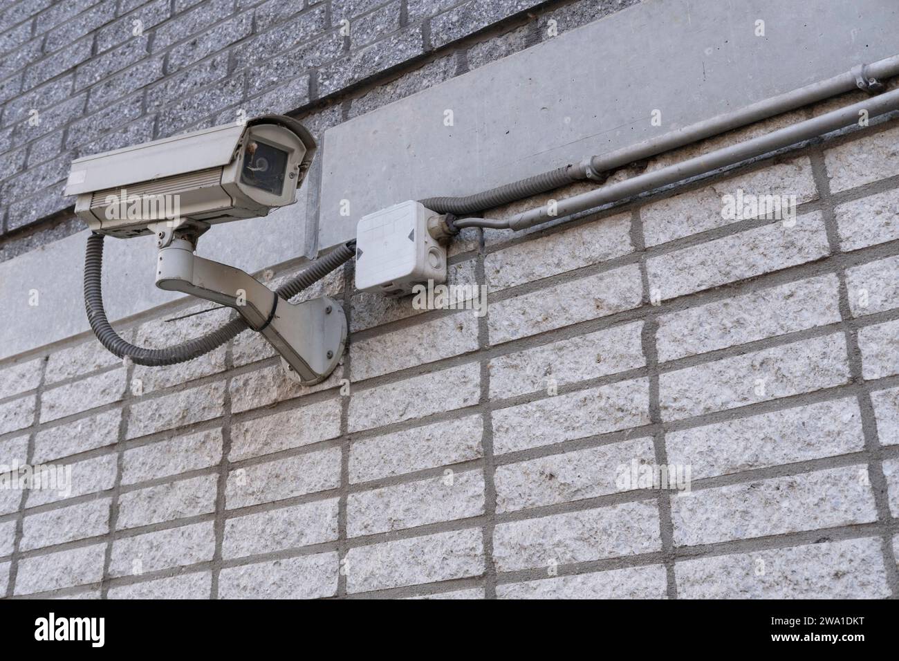 A somewhat dirty surveillance camera mounted on a wall to oversee the street Stock Photo