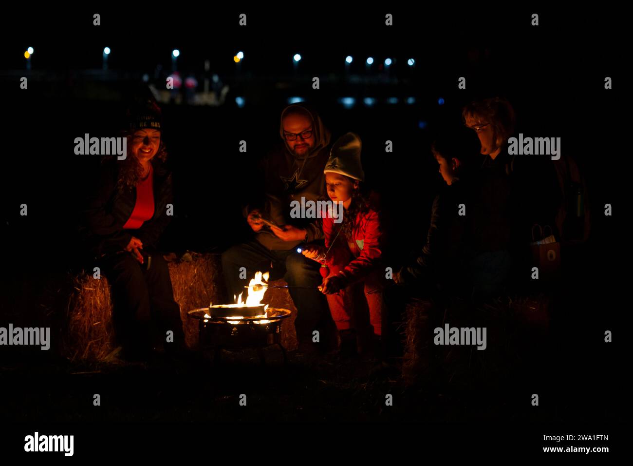 Des Moines, Washington, USA. 31st December, 2023. A family toasts marshmallows at the Burning Boat Festival at Des Moines Beach Park. People were invited to write notes of personal goals for the new year or sorrows that need purging that will be placed in the boat. Credit: Paul Christian Gordon/Alamy Live News Stock Photo