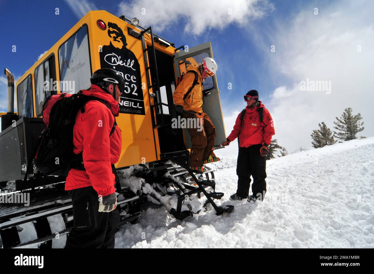 Two instructors greet a man exiting a snow cat while cat skiing at a mountain resort, California. Stock Photo