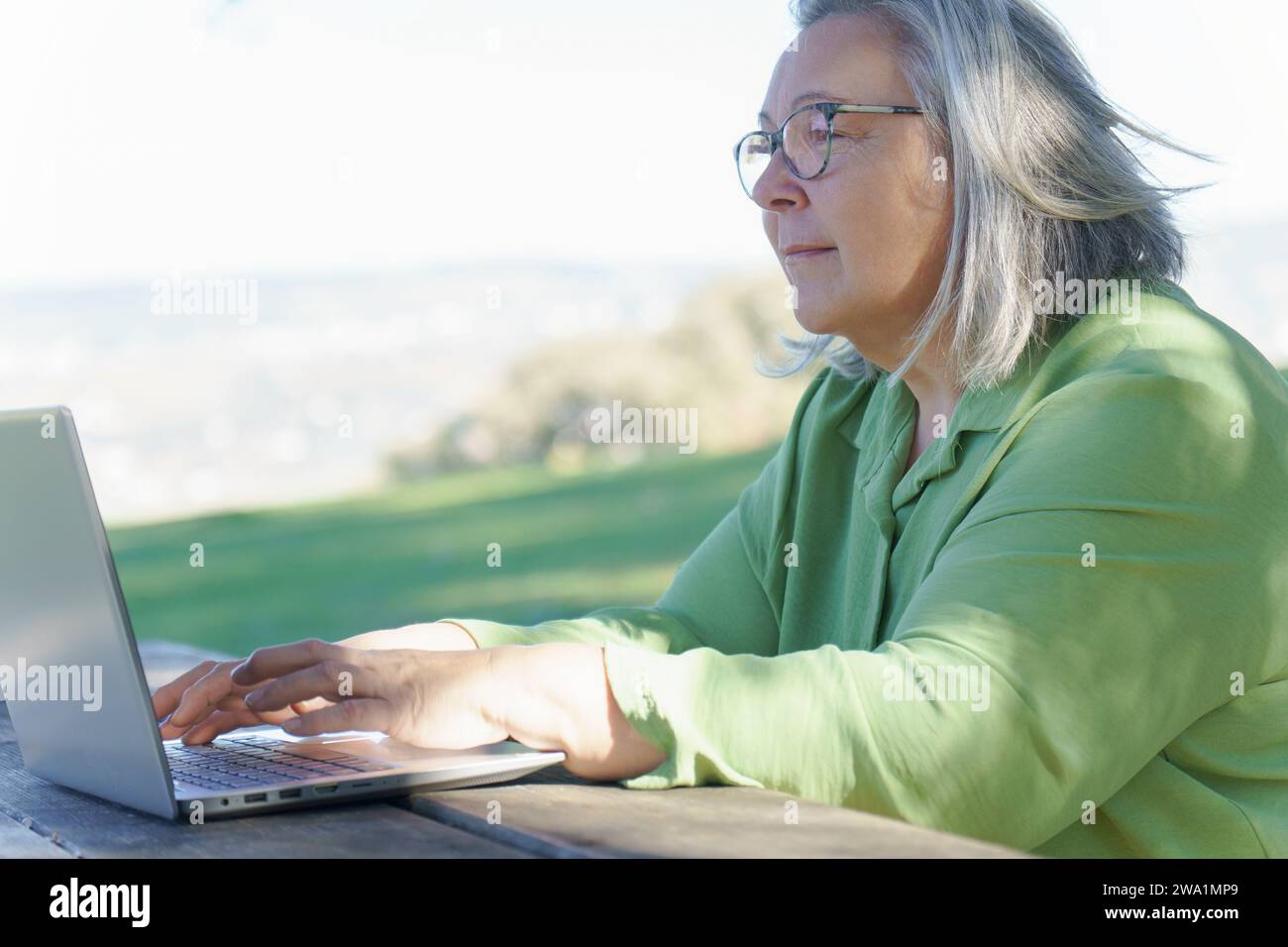 mature woman with white hair  smiling as she works at her computer Stock Photo