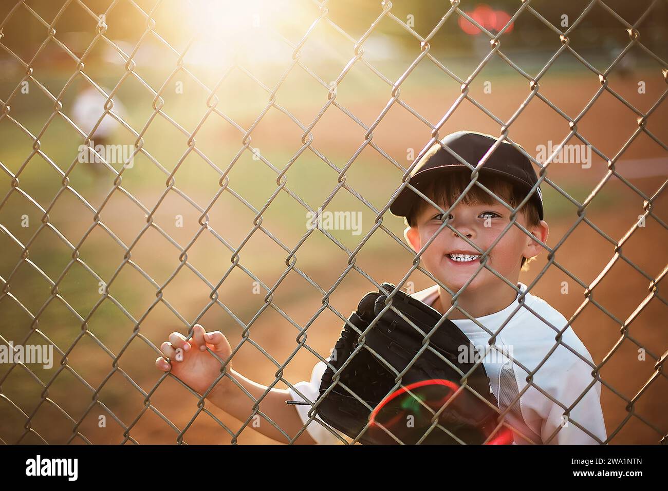 Little boy at a baseball game looking through the fence smiling Stock Photo