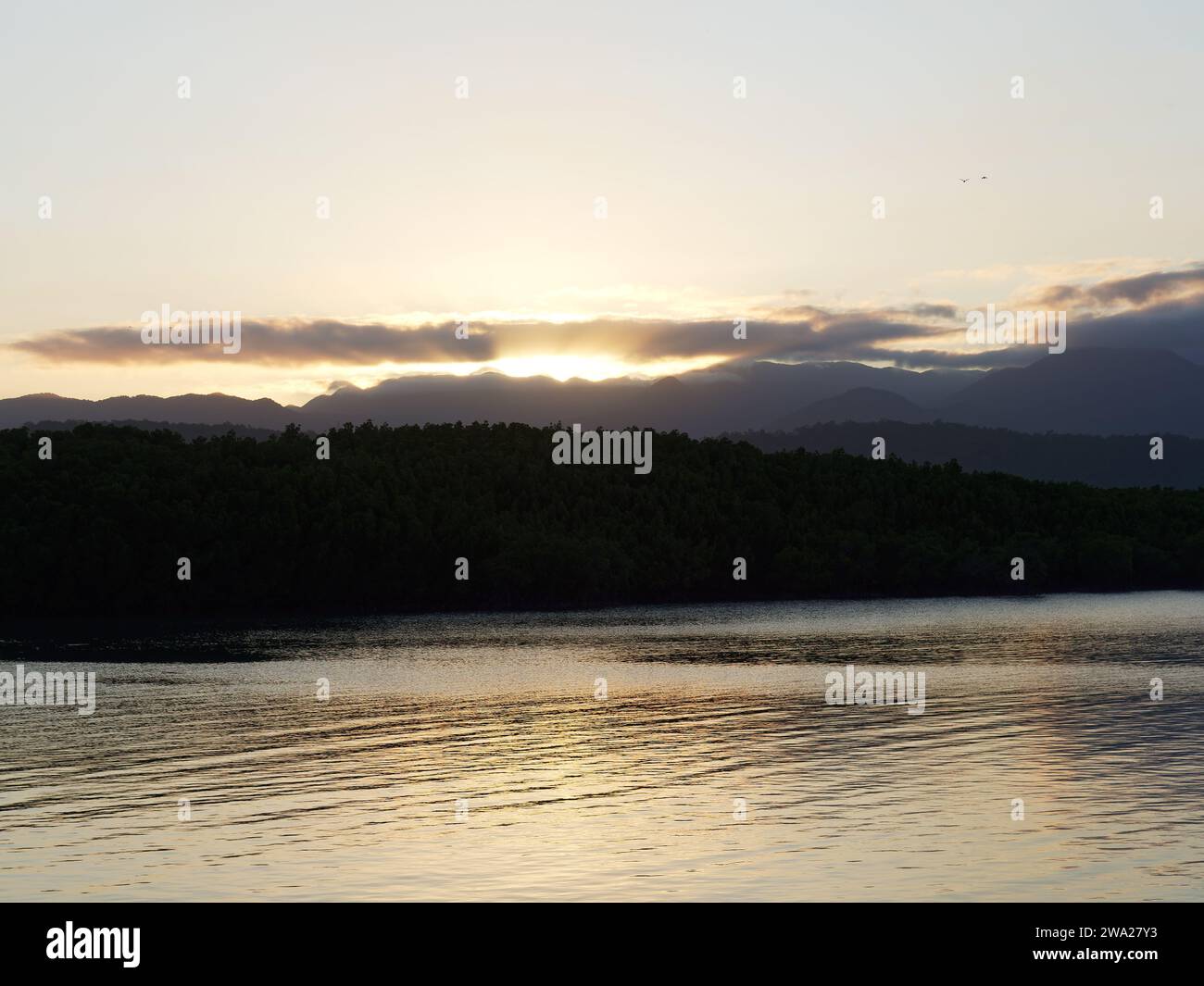 View of the sun setting over the distant hills in Port Douglas Queensland Australia Stock Photo