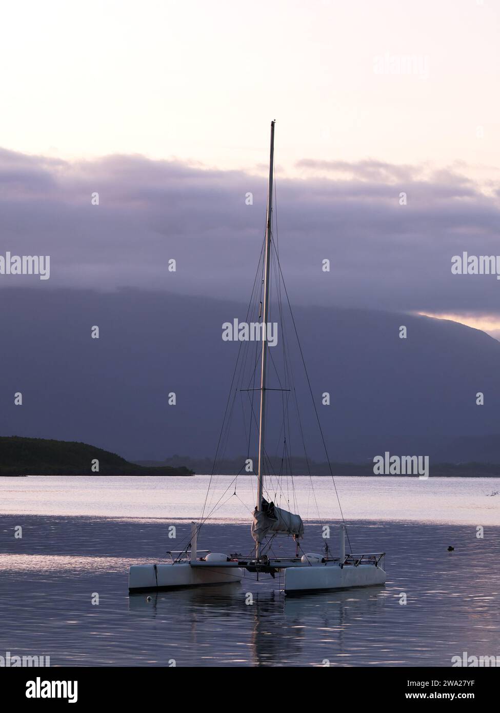 View of the sun setting over the distant hills and a catamaran moored in the foreground in Port Douglas Queensland Australia Stock Photo