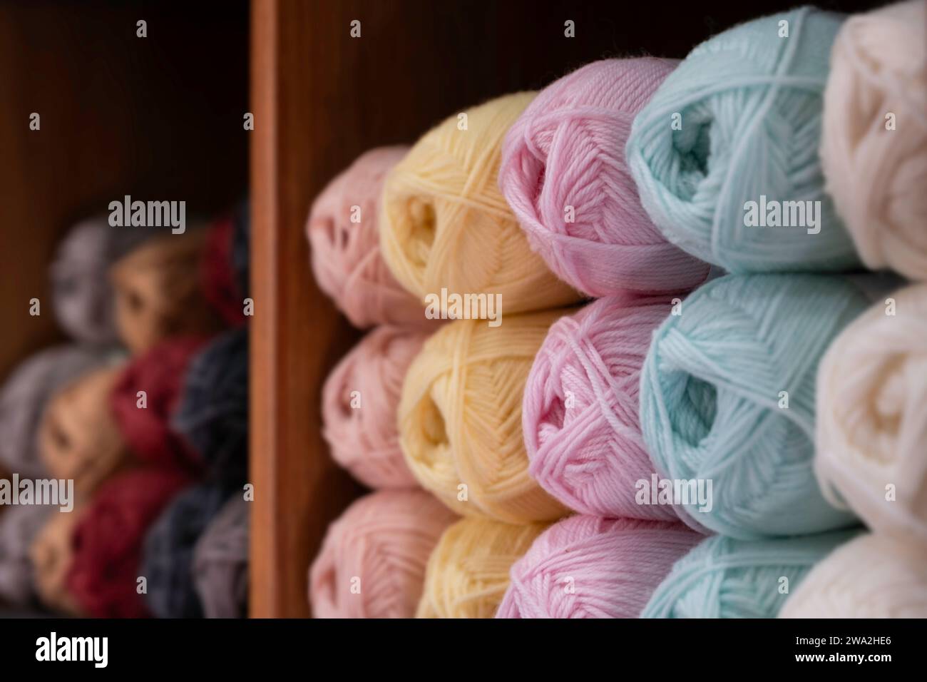 Balls of wool in various colors lie in a wooden cupboard in a shop. Narrow depth of field, focus on the pink spheres Stock Photo
