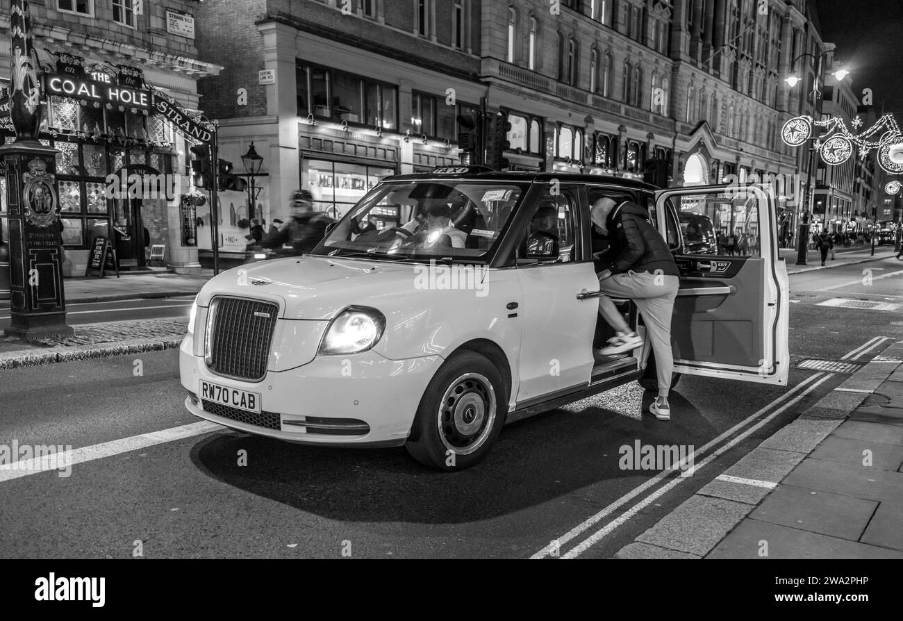 A person climbs into a white taxi cab in London England at night Stock Photo