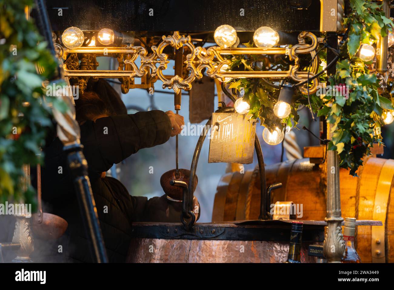 A woman ladling out Gluhwein (mulled wine) into a cup from a hot copper cauldron at Winchester Cathedral Christmas market, Hampshire, UK Stock Photo