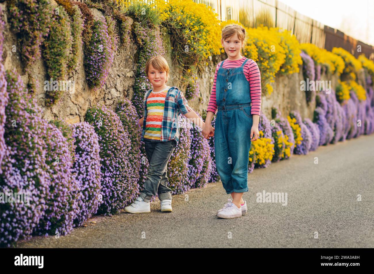 Two cute happy young kids playing together outdoors on a nice sunny evening, holding hands. Small brother and big sister spending time together Stock Photo