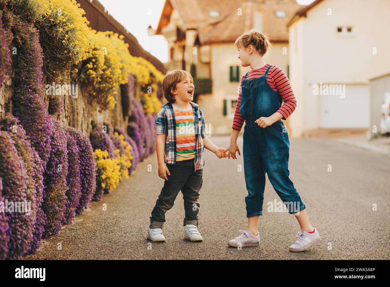Two cute happy young kids playing together outdoors on a nice sunny evening, holding hands. Small brother and big sister spending time together Stock Photo