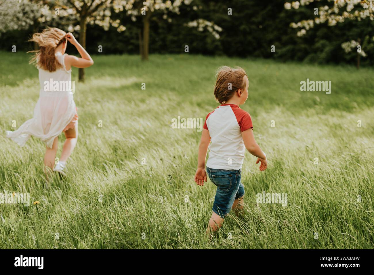 Two adorable kids playing together in spring garden on a very windy day, family spending time outdoors Stock Photo
