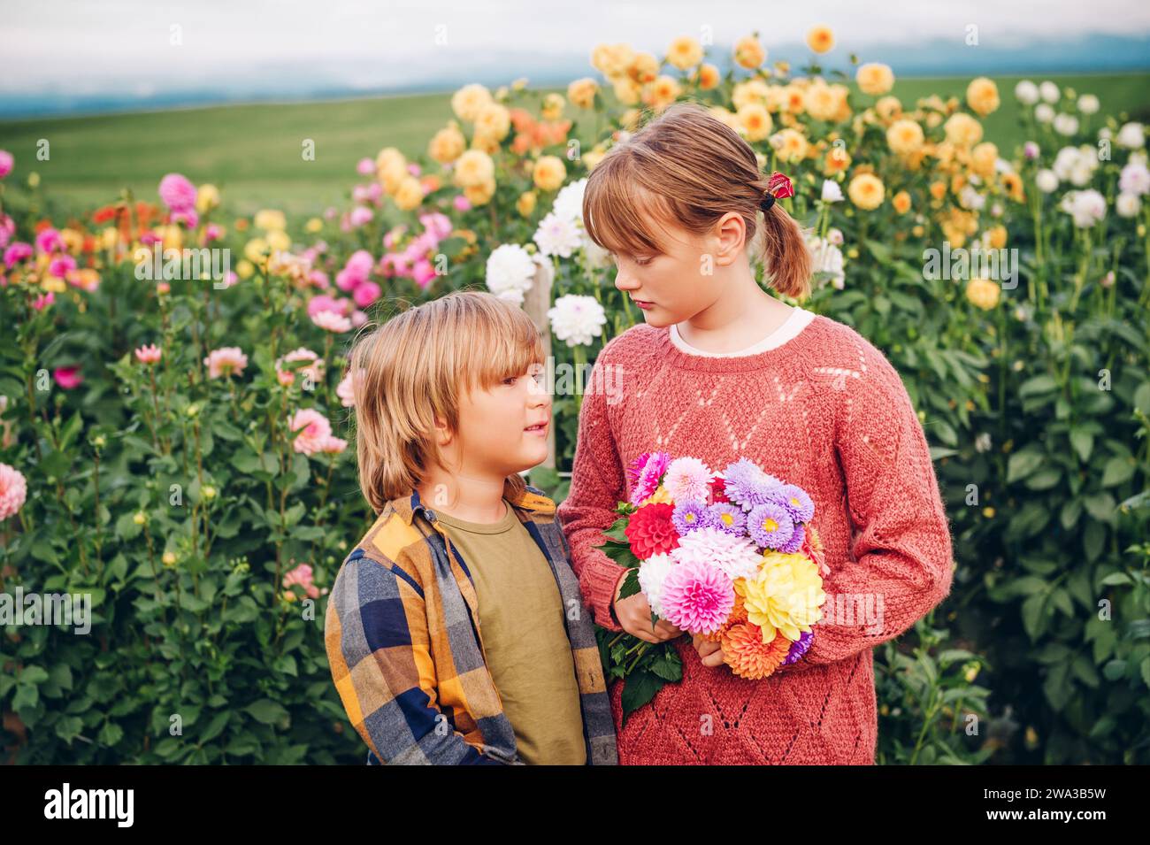 Outdoor portrait of two funny kids plying in autumn garden, holding dahlia flowers bouquet Stock Photo