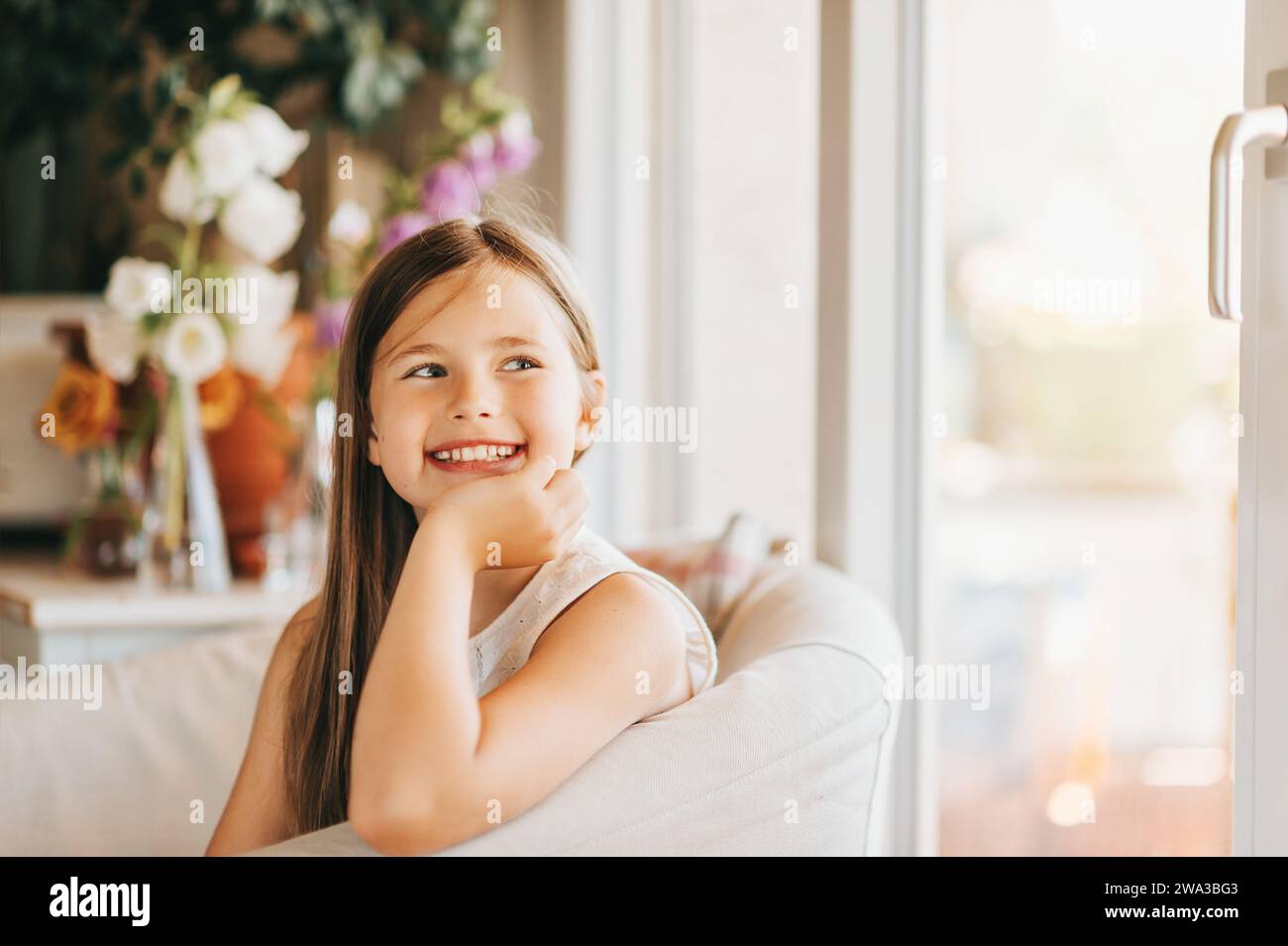 Cute little girl sitting in a white chair next to window at home Stock ...