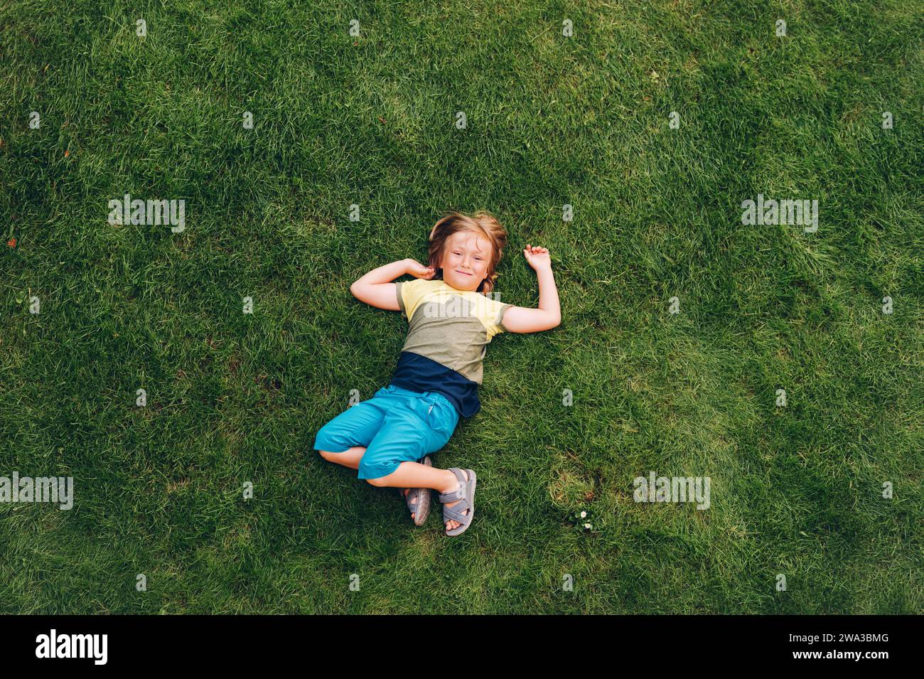 Happy child having fun outdoors. Kid playing in summer park. Little boy lying on green fresh grass, top view Stock Photo