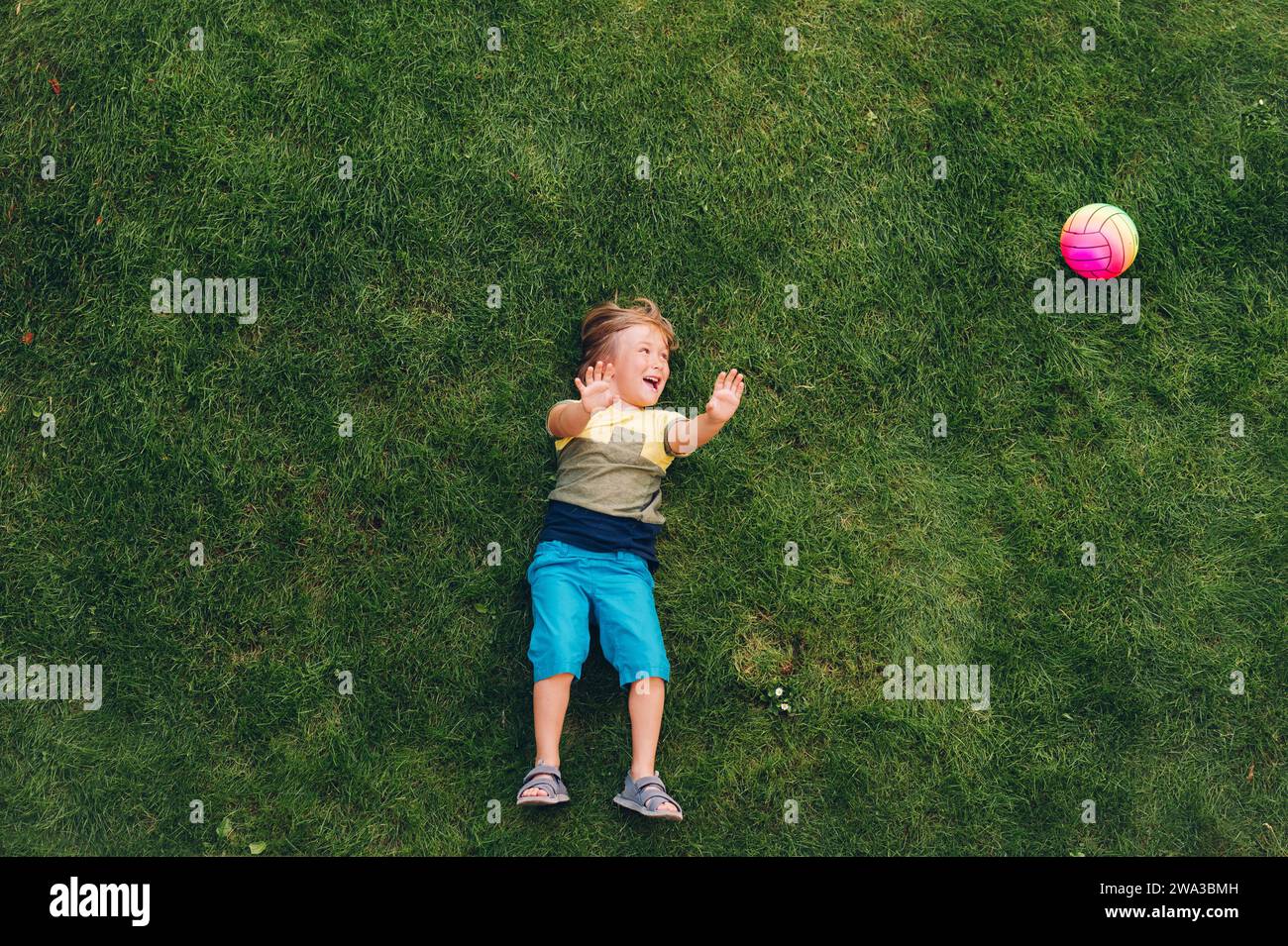 Happy child having fun outdoors. Kid playing in summer park. Little boy lying on green fresh grass, top view Stock Photo